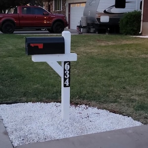 May include: A white mailbox post with a black mailbox and the house number 634 on the post. The mailbox is on a bed of white gravel.