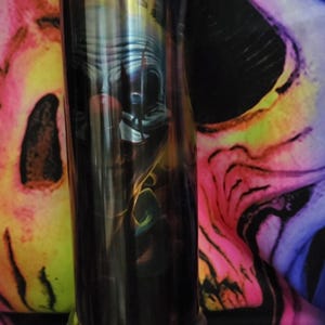 May include: A stainless steel tumbler with a black and white image of a clown with a red nose. The tumbler has a silver base and is sitting on a colorful background.