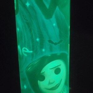 May include: A green glow-in-the-dark cylindrical lamp with a cartoon image of a girl with black hair and a boy with a mustache. The lamp has a white background with stars and bats.
