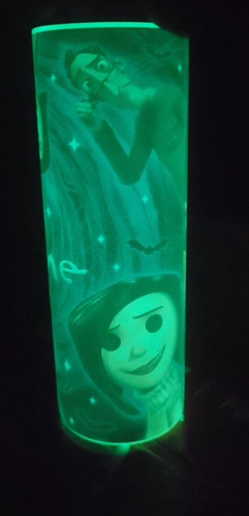 May include: A green glow-in-the-dark cylindrical lamp with a cartoon image of a girl with black hair and a boy with a mustache. The lamp has a white background with stars and bats.