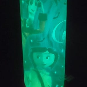 May include: A green glow-in-the-dark cylindrical lamp with a Halloween-themed design featuring a girl with a witch hat, a crescent moon, and bats.