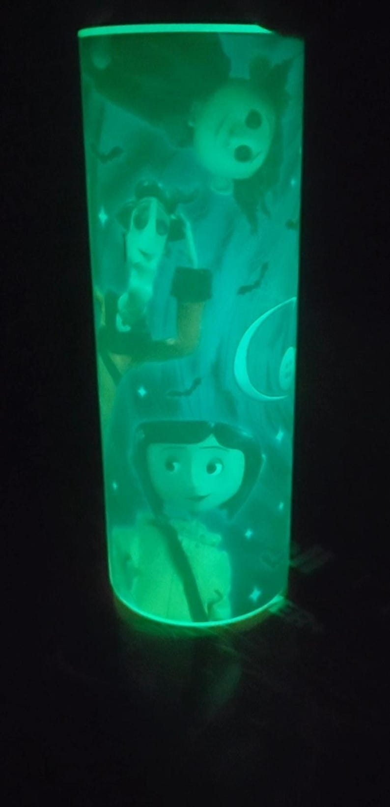 May include: A green glow-in-the-dark cylindrical lamp with a Halloween-themed design featuring a girl with a witch hat, a crescent moon, and bats.