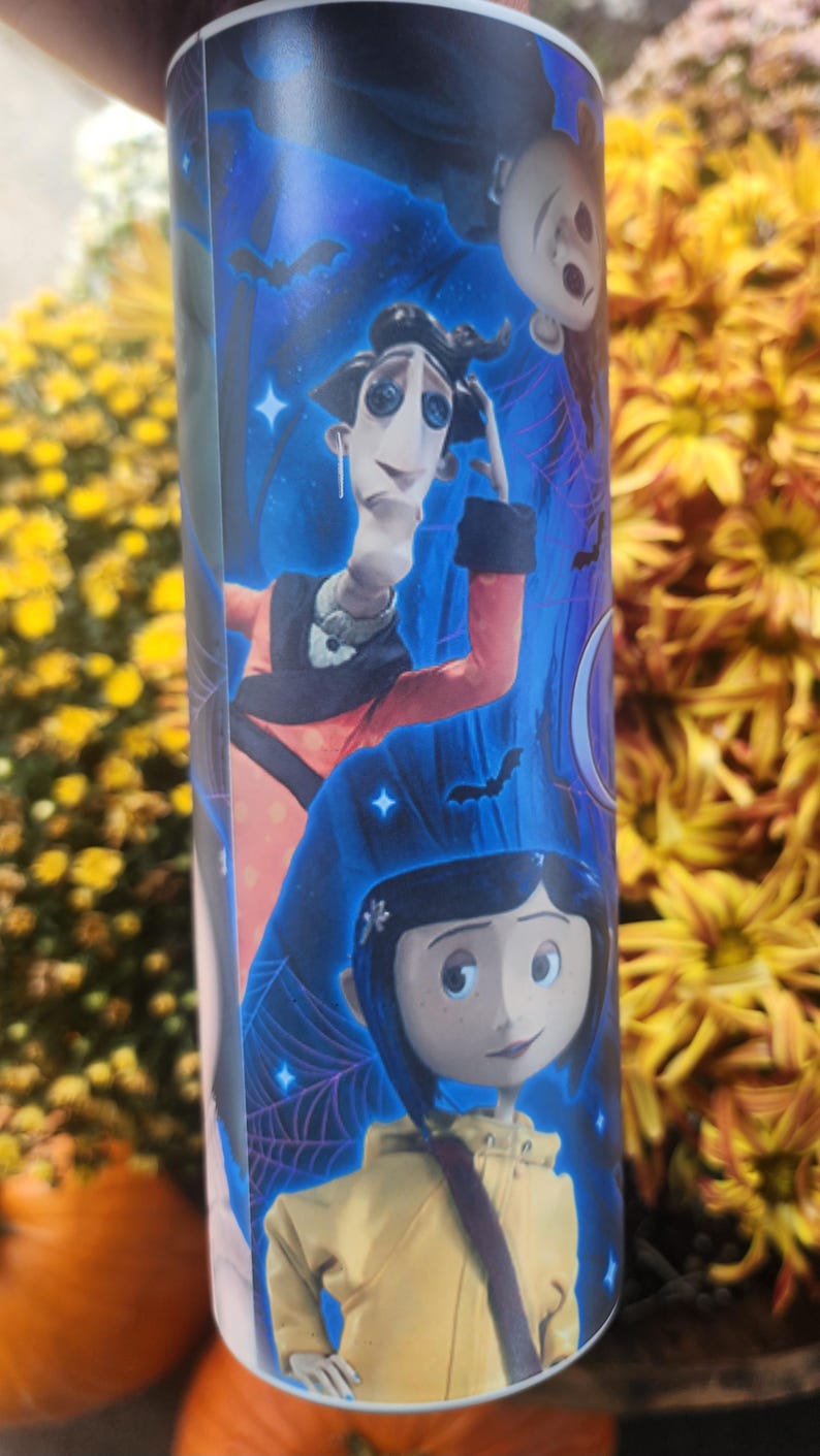 May include: A white tumbler with a blue, black, and purple background featuring characters from the movie "The Nightmare Before Christmas". The characters are Jack Skellington, Sally, and Oogie Boogie. The tumbler has a black lid.
