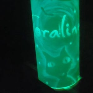 May include: A green glow-in-the-dark glass bottle with a black cat and the word "Coraline" written on it.