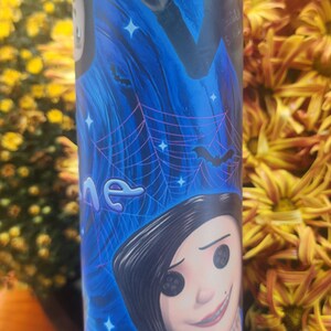 May include: A blue and black tumbler with a graphic of characters from the movie "The Nightmare Before Christmas". The characters include Jack Skellington and Sally. The tumbler has a black lid and a white bottom.