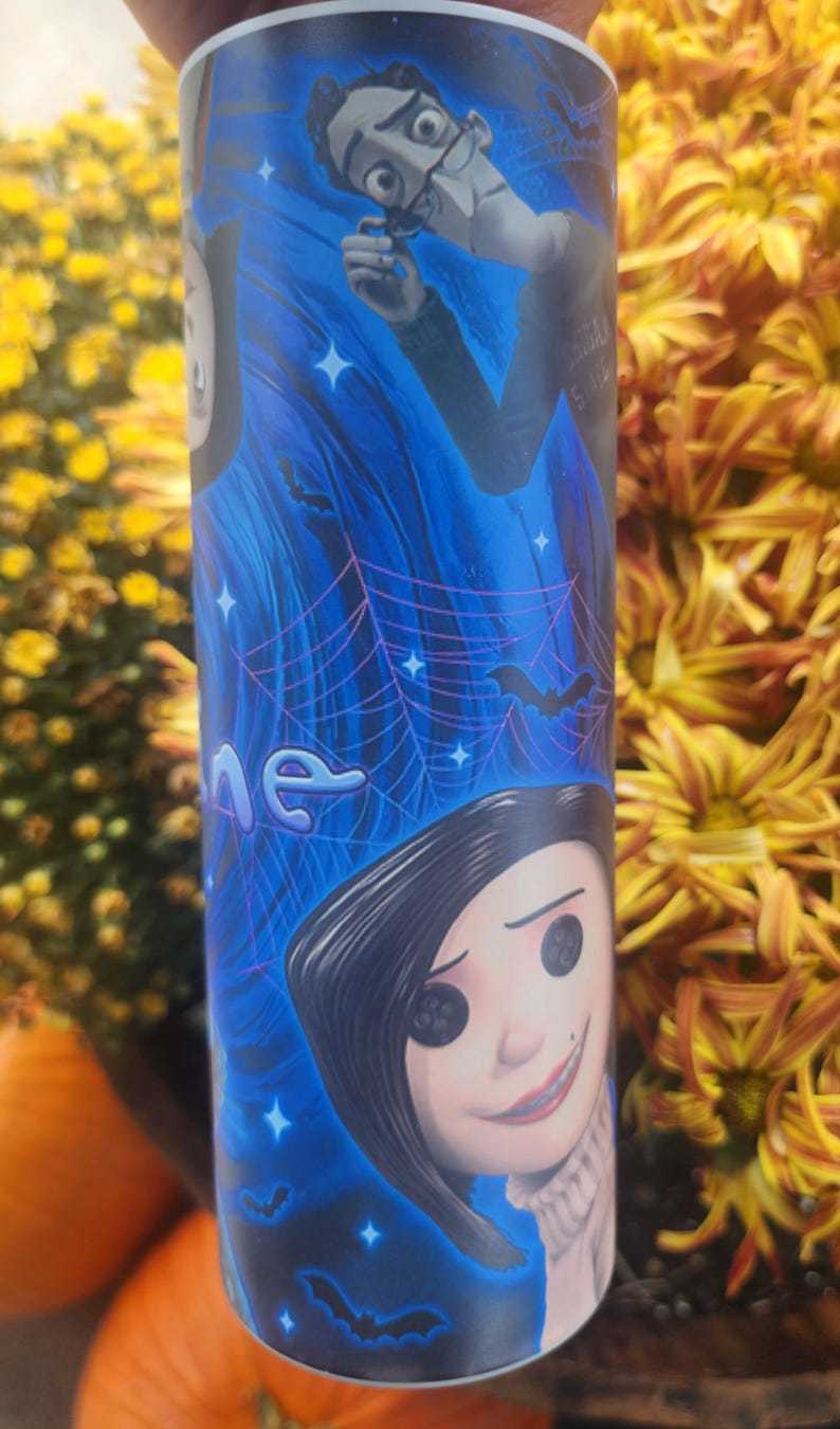 May include: A blue and black tumbler with a graphic of characters from the movie "The Nightmare Before Christmas". The characters include Jack Skellington and Sally. The tumbler has a black lid and a white bottom.