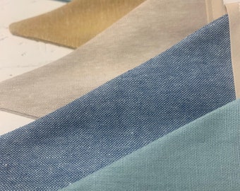 Peut inclure: Un ensemble de fanions en tissu dans différentes nuances de bleu et de beige. Les fanions sont faits d'un tissu texturé et sont disposés en quinconce.