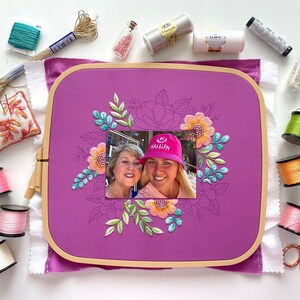 Op de afbeelding: Een paarse borduurring met een foto van twee vrouwen, omringd door bloemenborduurwerk in oranje, turquoise en groen. Het beeld wordt omringd door spoelen garen, naalden en scharen, wat duidt op een knutselproject.