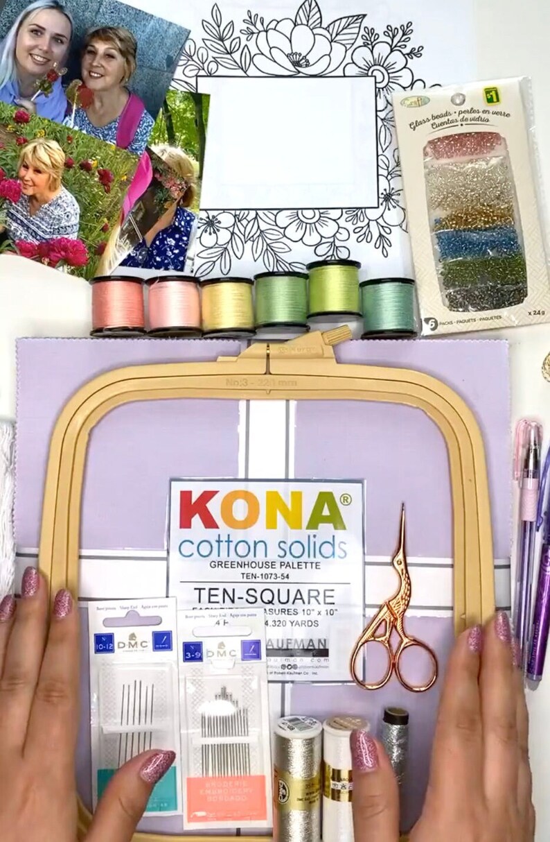 Op de afbeelding: Een platte lay-out van knutselbenodigdheden met borduurgaren, naalden, een schaar, een borduurring en stof. De afbeelding bevat een verpakking glaskralen, een bloemenontwerp en een kleurenkaart. De items zijn gerangschikt op een lichtpaars oppervlak.