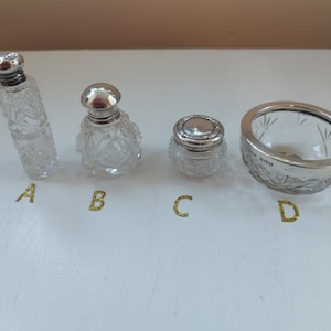 Pode incluir: Quatro garrafas de vidro transparente com tampas prateadas. As garrafas são decoradas com desenhos de vidro cortado. As garrafas estão dispostas em fila sobre uma superfície branca.