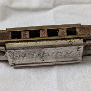 May include: A silver harmonica with the text "Hohner" and "Made in Germany" on the body. The harmonica has a brass top and bottom.