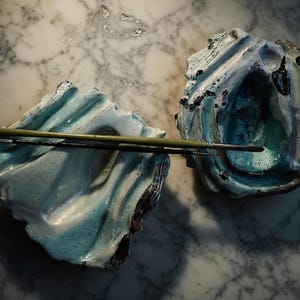 Può includere: Due ciotole in ceramica fatte a mano con un design strutturato e organico nei toni del blu e del bianco. Due pennelli poggiano sulle ciotole. Le ciotole sono su una superficie di marmo.