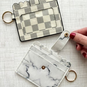 May include: Two white card holders with key rings. One has a chequered pattern and the other has a marble pattern.