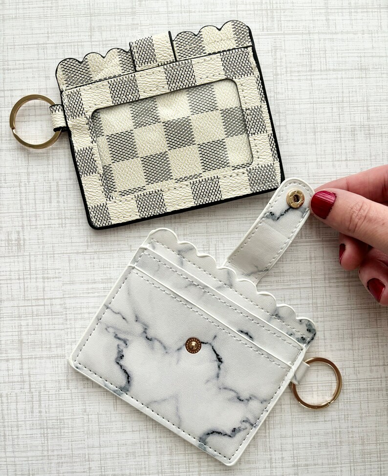 May include: Two white card holders with key rings. One has a chequered pattern and the other has a marble pattern.