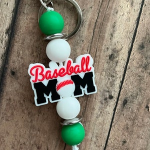 May include: A green, white, and black baseball mom keychain with a baseball graphic. The keychain has a silver ring and a white string.
