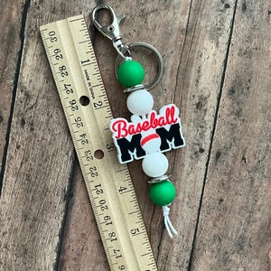 May include: A green, white, and black baseball mom keychain with a baseball graphic and the text "Baseball Mom".