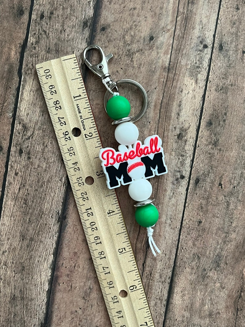 May include: A green, white, and black baseball mom keychain with a baseball graphic and the text "Baseball Mom".