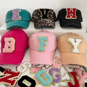 May include: Six different colored baseball caps with felt letters on the front. The letters are B, F, H, Y, E, and V. The caps are all distressed and have a vintage look.