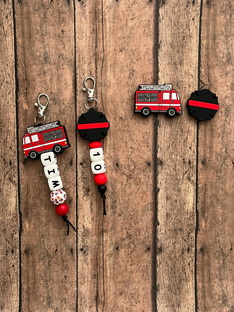 May include: Two red fire truck keychains with black and red beads. One keychain has the name "TIM" on it and the other has the number "110".