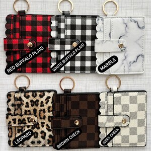 May include: Six different keychains with card holders. The keychains are in various patterns including red buffalo plaid, white buffalo plaid, marble, leopard, brown check, and ivory check.