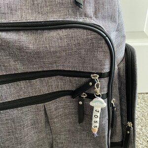May include: A gray backpack with black accents and a zipper pull with a rainbow charm and the name "JOSS" spelled out on it.