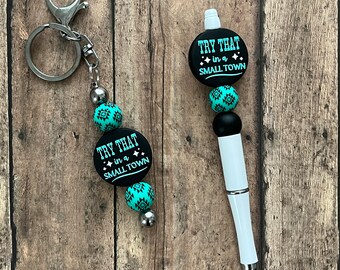 May include: A black and turquoise beaded keychain with a silver clasp and a round charm that says "Try That in a Small Town". A white pen with a black and turquoise beaded top and a round charm that says "Try That in a Small Town".