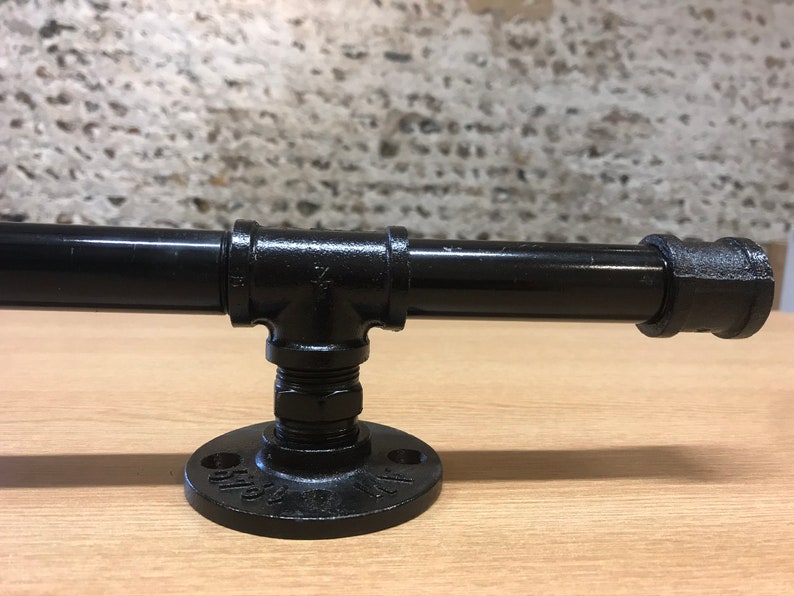May include: Black metal pipe fitting with a flange and a threaded pipe. The pipe fitting is mounted on a wooden surface.