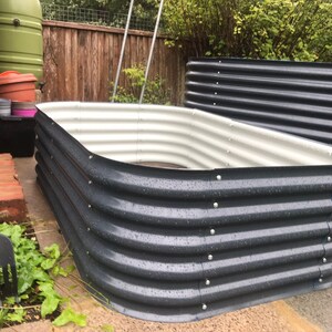 May include: A raised garden bed made of corrugated metal with a white interior. The bed is empty and appears to be ready for planting.