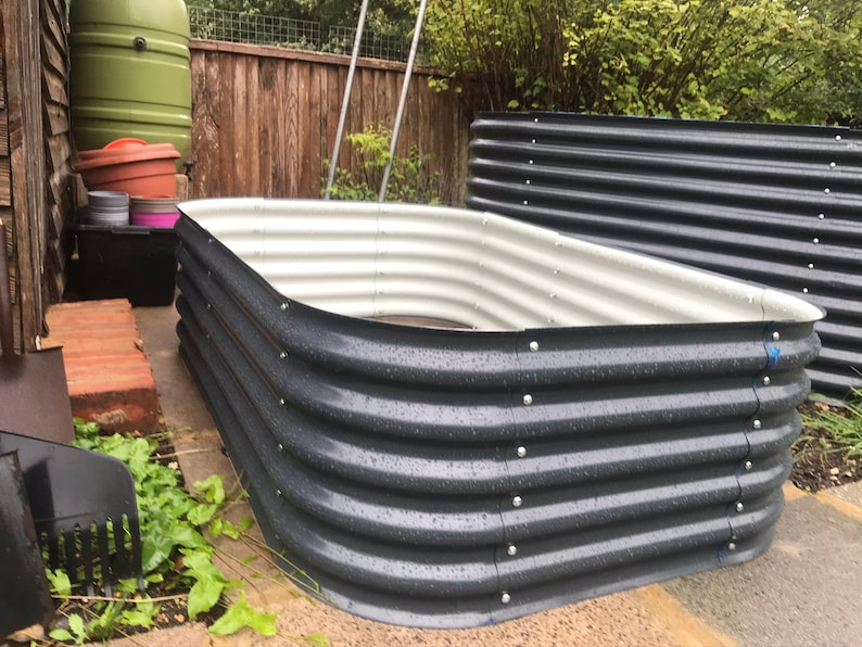 May include: A raised garden bed made of corrugated metal with a white interior. The bed is empty and appears to be ready for planting.
