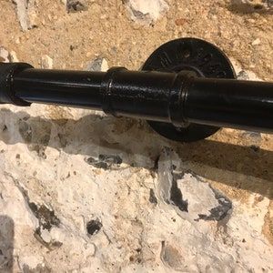 May include: Black metal pipe handrail with a black metal flange mounted to a stone wall.
