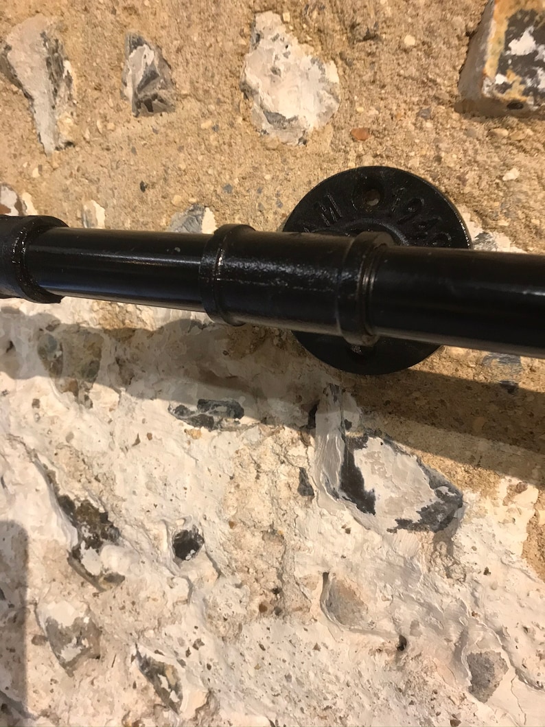 May include: Black metal pipe handrail with a black metal flange mounted to a stone wall.