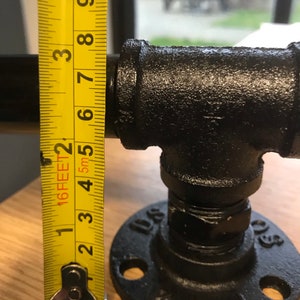 May include: Black metal pipe fitting with a flange and a measurement tape showing 3 inches. The pipe fitting is used for plumbing or industrial applications.