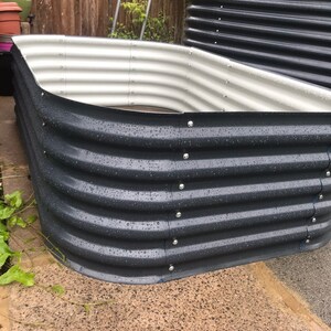 May include: A dark gray metal raised garden bed with a white interior. The bed is made of corrugated metal and has a rounded shape. The bed is wet from rain.