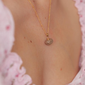 May include: A gold chain necklace with a small, light brown, irregularly shaped pendant.