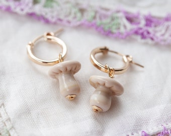 May include: A pair of gold hoop earrings with a white mushroom charm hanging from each hoop.