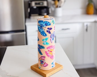 May include: A wooden paper towel holder with a roll of paper towels featuring a colorful butterfly pattern. The paper towels are pink with blue, green, yellow, and purple butterflies.