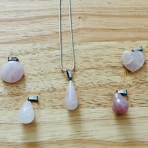 May include: A set of six rose quartz pendants in various shapes, including a teardrop, heart, and round shapes. The pendants are strung on silver chains and are ready to be worn as necklaces.