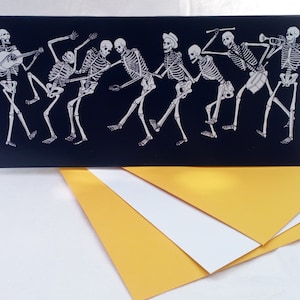 May include: A black card with a white illustration of a band of skeletons playing musical instruments. The skeletons are dancing and having fun. The card is perfect for a Halloween party or a spooky occasion.