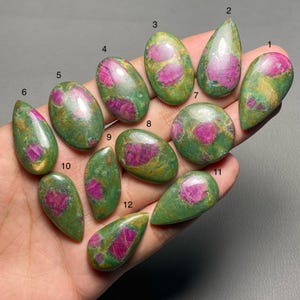 Puede incluir: Una colección de doce piedras preciosas de rubí en zoisita en varias formas. Las piedras presentan una vibrante mezcla de zoisita verde e inclusiones de rubí rosa intenso. Cada piedra pulida muestra patrones y colores naturales.