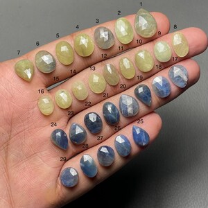 Puede incluir: Una variedad de piedras preciosas en tonos amarillos y azules. Las piedras están facetadas y vienen en varias formas, incluyendo ovaladas, de pera y de lágrima. Las piedras están numeradas del 1 al 29.