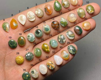 May include: A selection of 35 polished gemstones in diverse shapes and colours, including oval, teardrop, and round. The gemstones display patterns of green, brown, orange, and white. Each stone is numbered for identification.