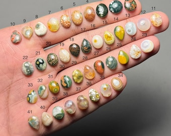 May include: A selection of 41 polished gemstone cabochons, featuring diverse colours and patterns such as brown, green, yellow, and white. Each stone is numbered, displaying a range of shapes and textures, ideal for jewellery making or collecting.