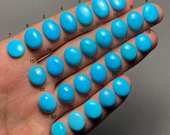 May include: A selection of 27 oval turquoise gemstones in various sizes and shades of blue. The gemstones are displayed on a hand, each stone numbered. The polished stones have a smooth, glossy surface, reflecting light. The gemstones are measured in cm.