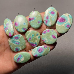 May include: Ten polished cabochon gemstones featuring a light green matrix with vibrant magenta and teal inclusions. Each stone is numbered from one to ten, displaying unique organic patterns and smooth, rounded surfaces in various shapes.