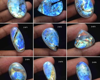 May include: Nine polished moonstone gemstones with iridescent blue and gold flashes. Each stone has a unique shape, including oval, teardrop, and triangular cuts. The gemstones are displayed against a dark background.