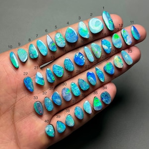Op de afbeelding: Een verzameling van veertig opalen in verschillende vormen en maten, elk met unieke patronen en kleuren. De opalen variëren van levendige blauw- en groentinten tot iriserende tinten, die de natuurlijke schoonheid van edelstenen laten zien. De opalen zijn genummerd van 1 tot 40.