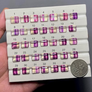 May include: A display of 34 rectangular fluorite gemstones, each with a unique pattern of purple and white stripes. The gemstones are arranged in rows and columns on a white background. The numbers 1 through 34 are printed above each gemstone.