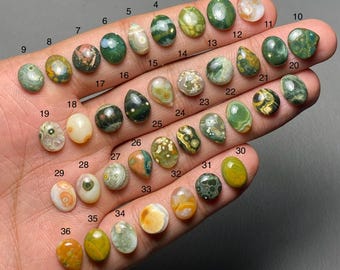 May include: A selection of 36 polished gemstones in diverse shapes and colours, including green, brown, yellow, and white. The gemstones are numbered 1 to 36 and are displayed on a hand.