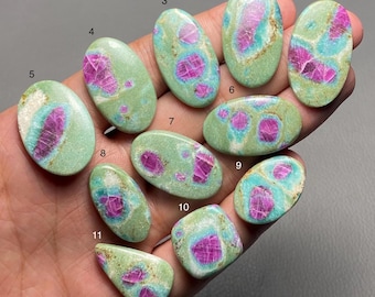 Può includere: Una collezione di undici pietre preziose lucide di varie forme, tenute in mano. Le pietre presentano un mix di colori, tra cui verde chiaro, turchese e magenta vibrante. Ogni pietra ha un motivo e una forma unici.
