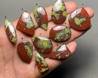 May include: A collection of ten polished gemstones in various shapes, including teardrop, oval, and triangular. The stones feature a mix of deep red and green hues, with a glossy finish. The gemstones are displayed against a neutral background.